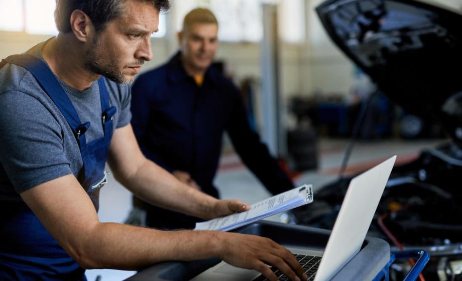 auto repairman working computer while doing car diagnostic with his coworker workshop