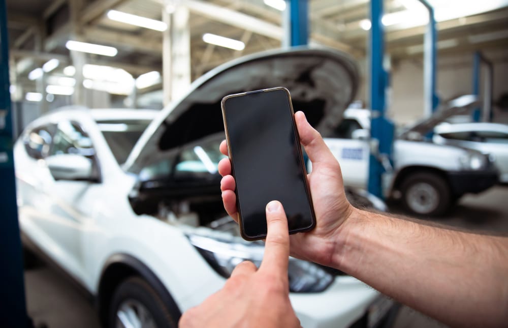 close up photo male hands with blank screen smartphone background auto service center with repairing cars