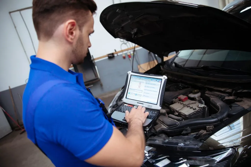 O NAMA - KDIJAGNOSTIKA obrt 7 young confident handsome car mechanic with laptop hand conducts computer diagnostics errors car systems